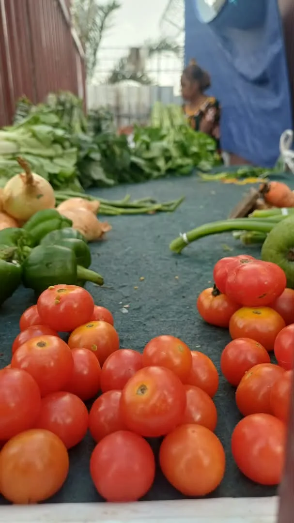 Fresh tomatoes, capsicum and greens laid out at a market stall